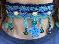 a woman wearing a blue crocheted neck piece with pearls and beads on it