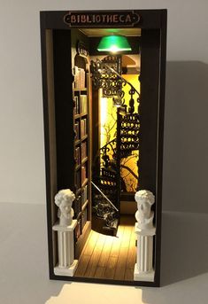 The diorama features a section of the library with tall bookshelves and a spiral wrought-iron staircase reaching to the ceiling. In the foreground there are busts of thinkers on pedestals, and behind the stairs there is a window behind which birds fly. Book Shelf Diorama, How To Make A Book Nook Shelf Insert, Library Book Nook Shelf Insert, 3d Book Nook, Cute Book Nooks, Bookshelf Nook Insert, Diorama Library