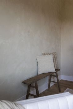 a wooden bench sitting in the corner of a room next to a white wall with a pillow on it