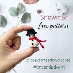 a hand holding a tiny snowman ornament on top of a white table