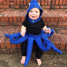 a baby in a blue octopus costume sitting on some bricks