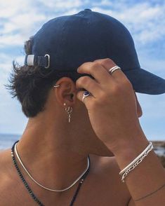 a man in a baseball cap looking at the ocean with his ear piercings on