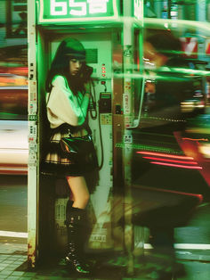 a woman is standing in a phone booth on the street with her hand on her hips