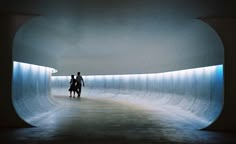 two people walking through a tunnel in the middle of an empty room with white walls