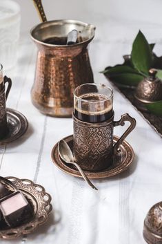 a table topped with two cups and saucers filled with liquid next to other dishes