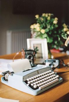 an old typewriter sitting on top of a wooden table next to a vase with flowers