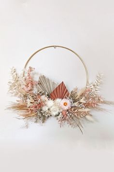 an arrangement of flowers and feathers in a circular metal frame on a white wall background