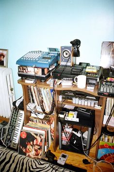 a room filled with electronics and pictures on top of a wooden shelf next to a bed