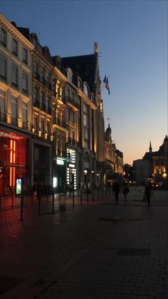 people are walking down the street in front of some buildings at night with lights on