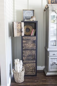 a tall wooden cabinet sitting on top of a hard wood floor next to a basket filled with books