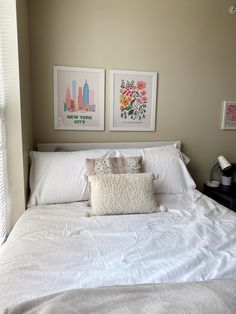 a bed with white sheets and two pictures on the wall above it's headboard