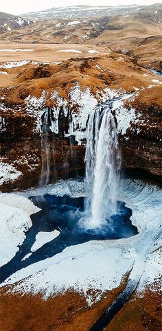 an aerial view of a large waterfall in the middle of snow covered ground and hills