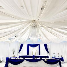 a white and blue wedding setup with draping on the ceiling, chandelier hanging from the ceiling