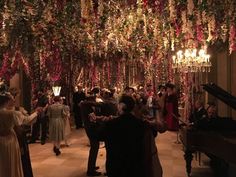 a group of people standing around a room filled with flowers and chandelier hanging from the ceiling