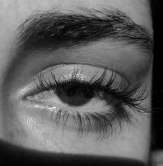 the eye of a man with long, thick lashes and no makeup is seen in this black and white photo