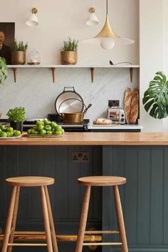 two wooden stools sit in front of an island with green fruit and vegetables on it