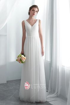 a woman standing in front of a window wearing a white dress and holding a bouquet