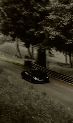 a black sports car driving down a road next to some tall trees in the background