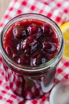 a jar filled with cherries sitting on top of a red and white checkered table cloth