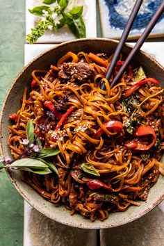 a bowl filled with noodles and meat on top of a white tablecloth next to chopsticks