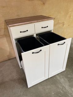 two black bins sit in the middle of a white cabinet with drawers on each side