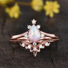 an opal and diamond ring sits on top of a piece of wood with yellow flowers in the background