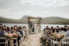 a bride and groom standing at the end of their wedding ceremony by the water with mountains in the background