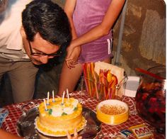 a man blowing out candles on a cake with other people around him looking at it