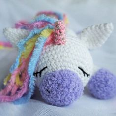 a crocheted stuffed unicorn laying on top of a white bed sheet with it's eyes closed