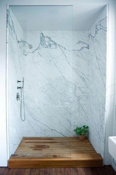 a bathroom with white marble walls and wood flooring, along with a walk in shower