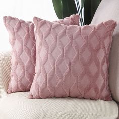 two pink pillows sitting on top of a white couch next to a potted plant