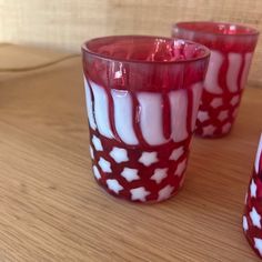 three red and white glass cups sitting on top of a wooden table next to each other