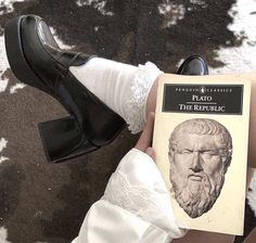 a person wearing white socks and black shoes is holding a book in their left hand