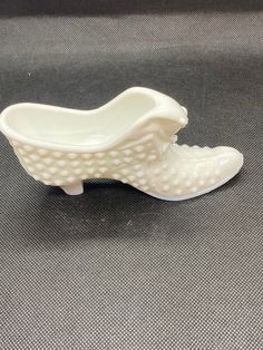 a white porcelain shoe shaped bowl sitting on top of a gray tablecloth covered floor