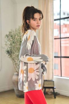 a woman standing in front of a window wearing leggings and a sweater with flowers on it