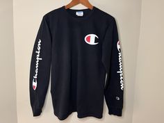 This is a black long sleeve athletic shirt featuring the Champion brand logo on the front and sleeves. It is made of 100% Cotton giving it a thick but comfortable feel. It is marked as a Men's Medium and fits True to Size. The shirt is in good vintage condition with no holes or tears - Please see photos.  Measurements laying flat: ~18 1/2 inches pit to pit ~24 inch sleeve ~27 inch length Black Long Sleeve T-shirt With Ribbed Cuffs, Black Long Sleeve Sweatshirt With Logo Print, Fall Sports Long Sleeve T-shirt, Black Long Sleeve Top With Logo, Winter Sports Long Sleeve T-shirt, Long Sleeve T-shirt For Streetwear, Long Sleeve Branding T-shirt For Streetwear, Sporty Long Sleeve T-shirt For Winter, Long Sleeve Athleisure T-shirt For Streetwear