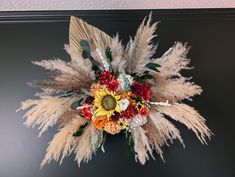 an arrangement of dried flowers and grasses on a wall in a room with black walls