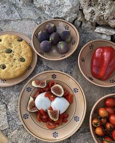 four bowls filled with different types of food on top of a stone floor next to some tomatoes and figs