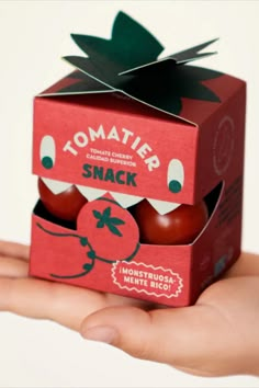 a hand holding a small red box with tomatoes in it that is shaped like a tomato