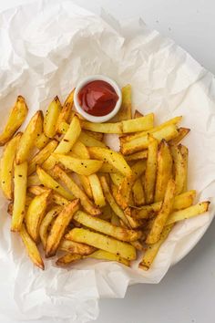 french fries with ketchup in a paper bowl on a white tablecloth covered plate