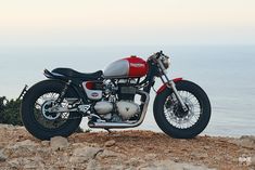 a red and white motorcycle parked on top of a rocky hill next to the ocean