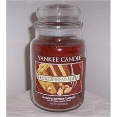 yankee candle with gingerbread maple inside on white table cloth next to glass jar filled with liquid