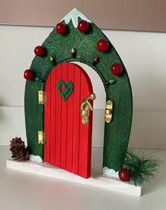 a red door is decorated with green and gold decorations for the holiday season in front of a pine cone tree