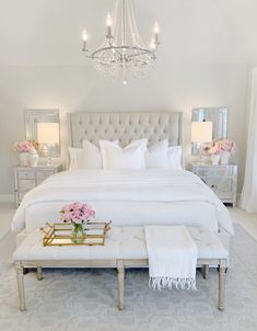 a white bed sitting in a bedroom next to a chandelier and two tables