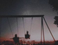 two people sitting on swings in front of a cityscape at sunset or dawn