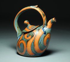 an orange and blue teapot with swirls on it's sides, sitting on a gray surface