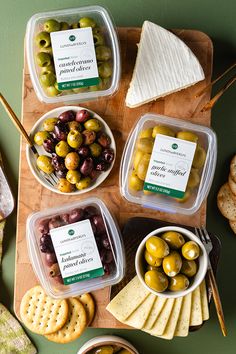 several containers of olives, cheese and crackers on a cutting board