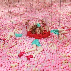 two women laying on the ground surrounded by pink and white balls, with mirrors in the background