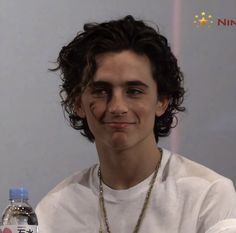 a young man with curly hair is holding a water bottle and smiling at the camera