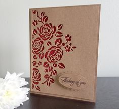 a white flower sitting on top of a table next to a brown card with red flowers